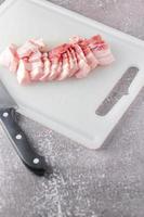 streaky pork is sliced on a white chopping board in the kitchen.Close up cutting slide pork belly raw photo