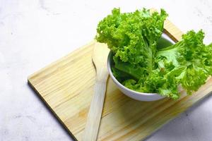 Lettuce placed in a white bowl and a cutting board on a white table. Vegetable salad. Vegetarian food. Clean food. Green vegetables. photo