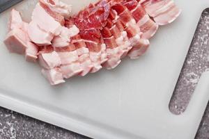 streaky pork is sliced on a white chopping board in the kitchen.Close up cutting slide pork belly raw photo