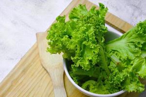 lechuga colocada en un tazón blanco y una tabla de cortar sobre una mesa blanca. ensalada de vegetales. comida vegetariana. comida limpia vegetales verdes.