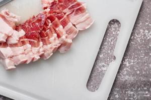 streaky pork is sliced on a white chopping board in the kitchen.Close up cutting slide pork belly raw photo