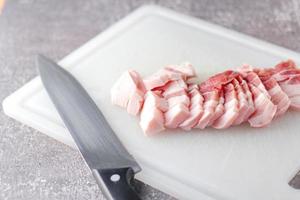 streaky pork is sliced on a white chopping board in the kitchen.Close up cutting slide pork belly raw photo