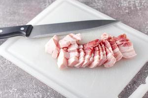 streaky pork is sliced on a white chopping board in the kitchen.Close up cutting slide pork belly raw photo