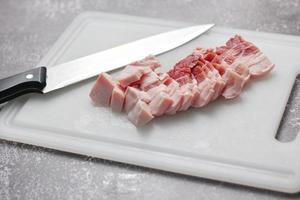 la carne de cerdo rayada se corta en rodajas en una tabla de cortar blanca en la cocina. foto