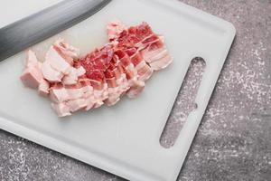 streaky pork is sliced on a white chopping board in the kitchen.Close up cutting slide pork belly raw photo
