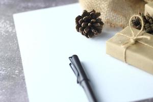 Holidays Gifts. Christmas and New Year.Gift box wrapped in brown paper pine cones and white paper and pens placed on the table, copy space. photo