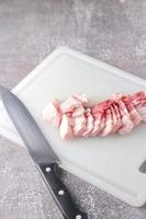 streaky pork is sliced on a white chopping board in the kitchen.Close up cutting slide pork belly raw photo