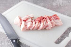 streaky pork is sliced on a white chopping board in the kitchen.Close up cutting slide pork belly raw photo