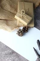 Holidays Gifts. Christmas and New Year.Gift box wrapped in brown paper pine cones and white paper and pens placed on the table, copy space. photo