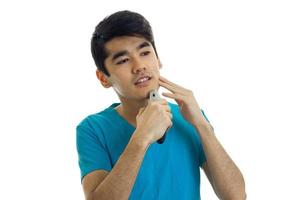 cute young guy with black hair looks ahead and carefully shaves his beard photo