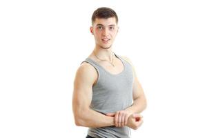 beautiful sporty guy stands in the grey t-shirt smiles and shows muscle on hand photo