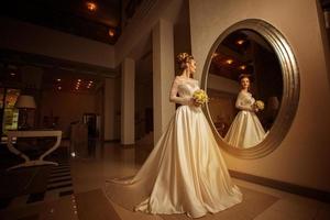 young bride in wedding dress looking at a big mirror photo