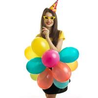 vertical portrait of a beautiful young girl who stands in front of the camera and holds sunglasses and lots of big balloons photo