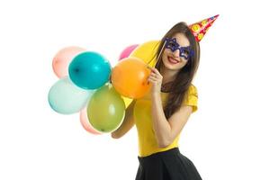 hermosa chica feliz con gafas con cono en la cabeza sostiene muchos globos y sonríe foto