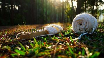 ein strickblock und ein weißer strickstoff mit garn auf gras vor natürlichem hintergrund und warmem sonnenlicht im park. video