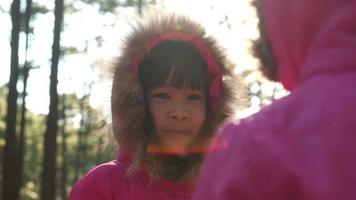 jolie petite fille dans un manteau d'hiver rose debout dans une forêt de pins souriant joyeusement à sa sœur. video