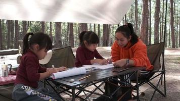 mutter und kleine tochter machen gemeinsam hausaufgaben im park. asiatische mutter bringt ihrer tochter bei, hausaufgaben zu lesen und zu schreiben. video