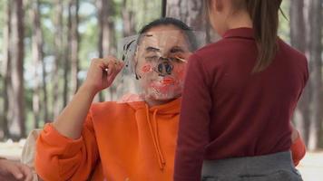 contento amorevole famiglia. Due poco ragazze dipinto loro La madre di viso con acquerelli. La madre di giorno. contento madre e bambino trascorrere inverno vacanze insieme nel un' pino foresta. video