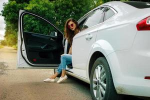 una dama glamorosa con anteojos se sienta en un gran auto blanco hermoso foto