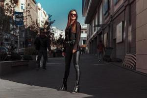 bella mujer con traje de cuero y gafas de sol posando en la ciudad foto