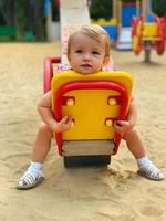 Cute little baby girl sits on a swing at the playground photo