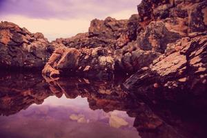 rocas y su reflejo en el mar al amanecer foto