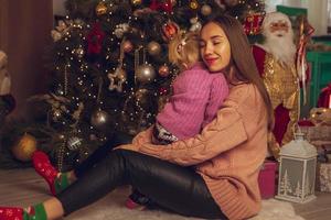 happy young mom hugs her little baby girl at the christmas tree photo
