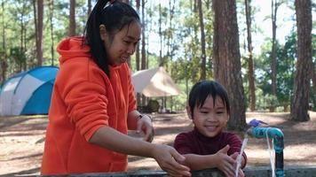 Young mother with little daughter in pajamas washes face and hands in morning at camping ground in pine forest , family spending time together on winter vacation. video