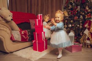 dos niñas pequeñas con un árbol de navidad por detrás en casa foto