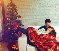 beautiful couple in love lies on a couch wrapped in plaid Christmas Eve photo