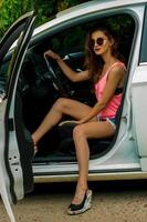 Sexy brunette woman driver sits by the drive wheel in a white car photo