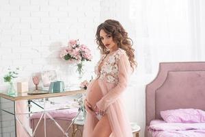 bella mujer embarazada con un vestido rosa en casa foto