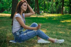 charming pretty girl sitting on the grass in the Park and listens to music photo