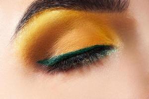 Closed woman eye with yellow makeup and green stripe photo