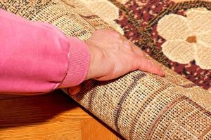 Repair, construction and house concept - close-up of female hands rolling up a carpet. photo