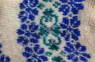 Background of white knitted fabric with blue-green handmade ornament from Argentine merino wool. photo