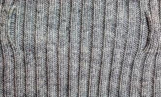 Gray knitted handmade sweater background. The texture of the surface of the woolen jersey made of yarn, close-up. Image for the background. Wool carpet or sweater. Gray texture. Modern design. photo