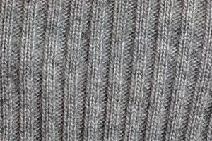 Gray knitted handmade sweater background. The texture of the surface of the woolen jersey made of yarn, close-up. Image for the background. Wool carpet or sweater. Gray texture. Modern design. photo