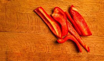 Fresh red capsicum pepper cut into slices on a wooden kitchen board. photo