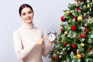 Woman with an alarm clock points her finger at dial, Christmas time concept photo