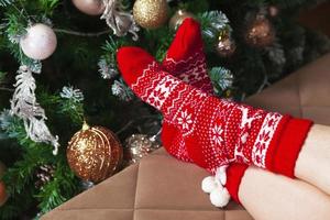 Female feet in red knitted socks and decorated Christmas tree photo