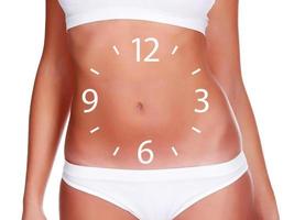 Slim woman body with a clock face on her belly on white background, isolated photo