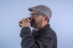 Portrait of 60 years old bearded man on blue background with hat and glasses photo