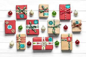 cajas de regalo rojas y verdes envueltas a mano decoradas con cintas, copos de nieve y números, adornos navideños y decoración en mesa blanca concepto de calendario de adviento de navidad vista superior tarjeta de vacaciones plana foto