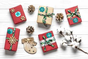 cajas de regalo rojas y verdes envueltas a mano decoradas con cintas, copos de nieve y números, adornos navideños y decoración en mesa blanca concepto de calendario de adviento de navidad vista superior tarjeta de vacaciones plana foto