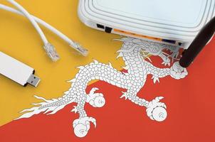 Bhutan flag depicted on table with internet rj45 cable, wireless usb wifi adapter and router. Internet connection concept photo