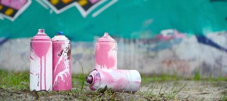 A few used paint cans lie on the ground near the wall with a beautiful graffiti painting in pink and green colors. Street art concept photo