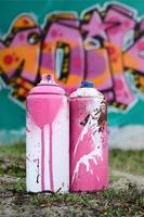 A few used paint cans lie on the ground near the wall with a beautiful graffiti painting in pink and green colors. Street art concept photo