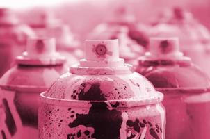 A lot of dirty and used aerosol cans of paint. Macro photograph with shallow depth of field. Selective focus on the spray nozzle Image toned in Viva Magenta, color of the 2023 year photo