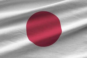 Japan flag with big folds waving close up under the studio light indoors. The official symbols and colors in banner photo